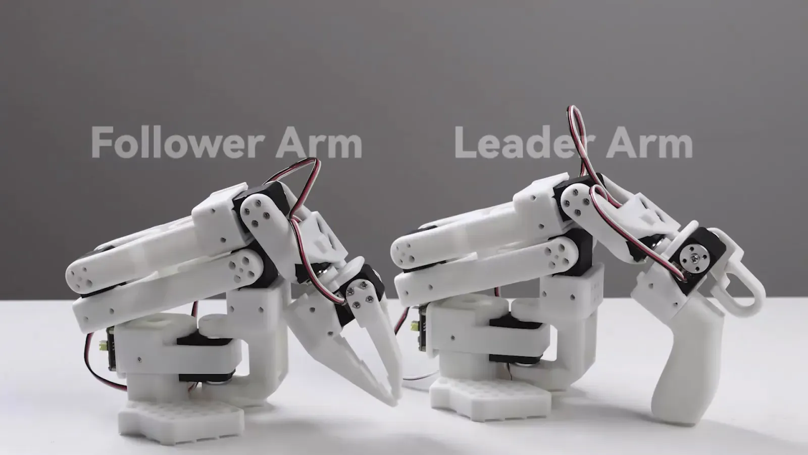 Two white tabletop robot arms configured for leader-follower teleoperation.